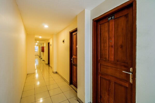 A hotel hallway with wooden doors, a tiled floor, and a bright ceiling light.