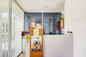 A reception area with a glass partition, a wooden counter, and various informational posters including hygiene and safety guidelines. - OYO 90230 Skyland Bogor Valley (Bogor)