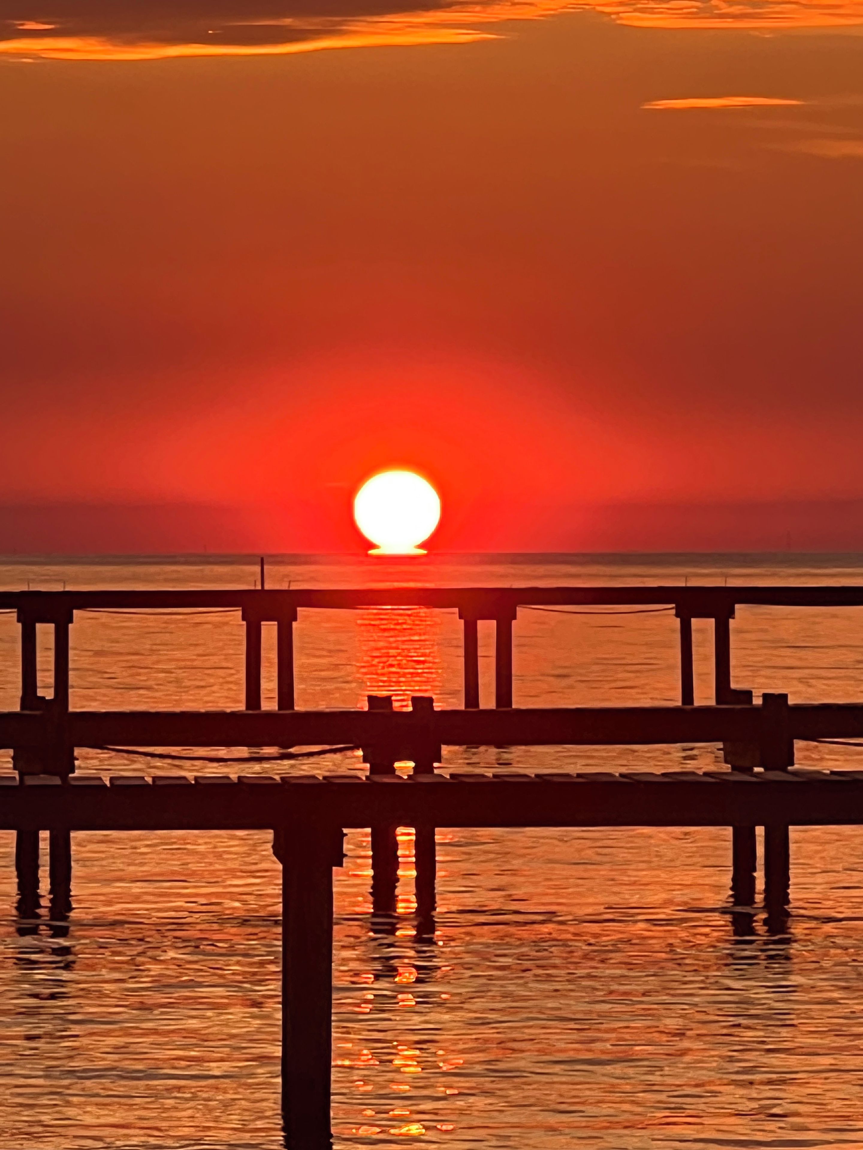 A sunset over a calm body of water with a wooden pier extending into the water.