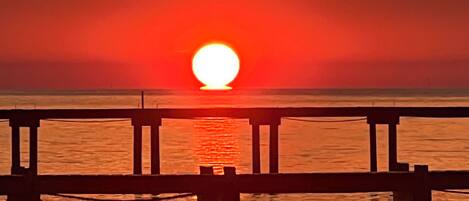 A sunset over a calm body of water with a wooden pier extending into the water.