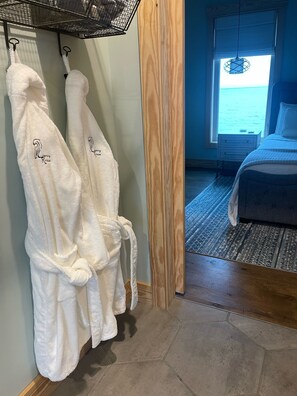 A hotel room with a bed, a wooden floor, and a view of the sea through a window.