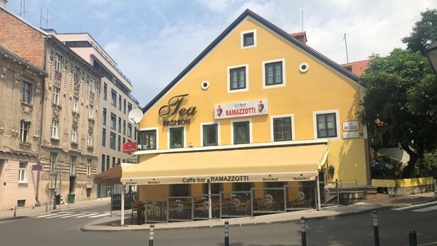 Ein gelbes Gebäude mit einem Schild für 'Tea Fashion' und 'Caffe bar RAMAZZOTTI' im Erdgeschoss.