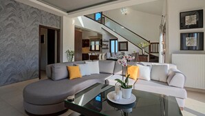 Un salon moderne avec un canapé d’angle, une table basse en verre et un escalier menant à un niveau supérieur.