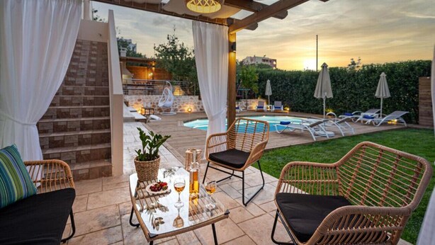 Un espace extérieur aménagé en terrasse, avec des meubles en osier, une table en verre et une piscine en arrière-plan.