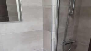 Um banheiro com vaso sanitário, chuveiro com porta de vidro e paredes revestidas de azulejos.