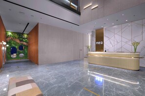 Eine moderne Lobby mit einer Rezeption, einem Marmorboden und einer grünen Wand mit Pflanzen.