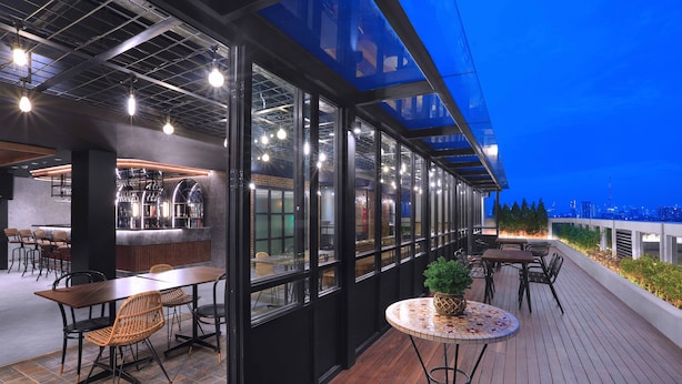 Un área de comedor al aire libre con mesas y sillas, un bar y vistas del horizonte de la ciudad al atardecer.