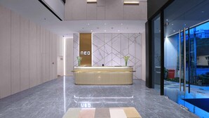 Un área de recepción moderna con suelo de mármol, un mostrador de recepción y una pared de vidrio con vistas al exterior.