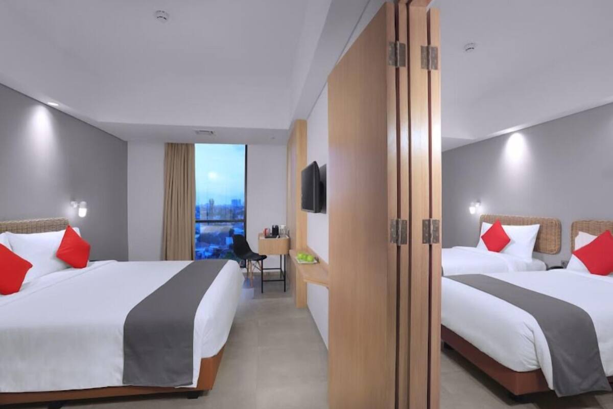 A hotel room with two beds, a desk, a chair, a TV, and a view of the city.