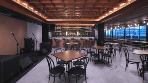 Zona de bar moderna con techo de madera, taburetes y un área de estar con mesas y sillas.