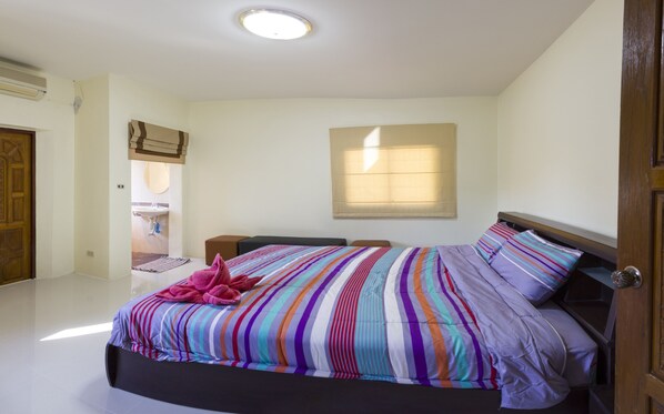 A bedroom with a bed, a window, a bedside table, and a door.