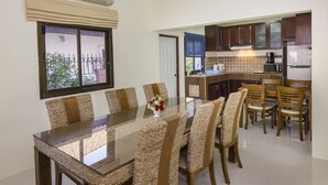 Un comedor con mesa de vidrio rodeada de sillas de mimbre, una cocina con armarios de madera y vistas al exterior por una ventana.