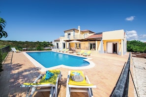 A poolside area with lounge chairs, a swimming pool, and a two-story house with a balcony.