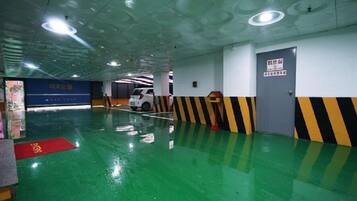 An indoor parking area with green flooring, a white car parked, and a blue sign with yellow text.