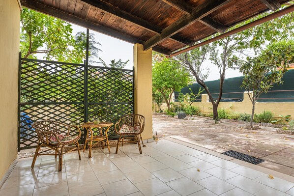 Un patio techado con suelo de baldosas, muebles de mimbre y un cerramiento de celosía.