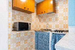 A compact kitchen with a microwave, sink, and gas stove. - Beautiful Cottage with Garden, Terrace and Wi-Fi; Parking Available (Quartu Sant'elena)