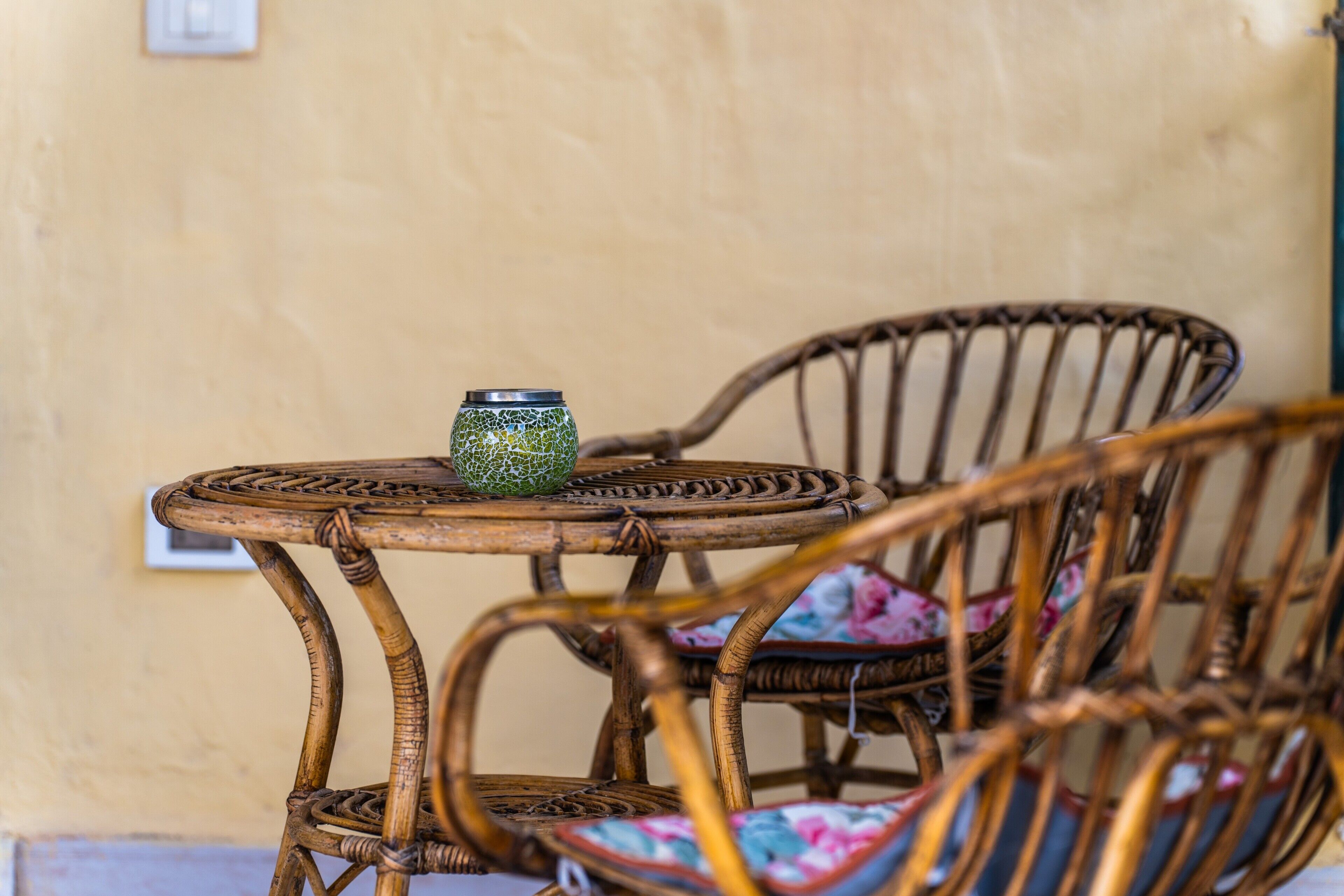 Mobili in vimini con un tavolino e sedie, un vaso decorativo e una parete con un interruttore.