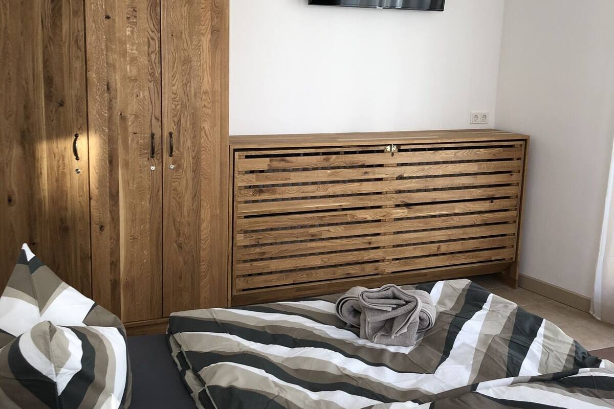 A bedroom with a bed, a wooden wardrobe, and a television mounted on the wall.