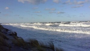Una playa con olas, dunas cubiertas de hierba y un cielo despejado.