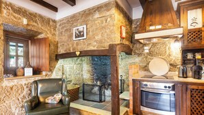 A stone-walled room with a fireplace, a leather chair, and a built-in oven. - Refúgio das Artes (Porto de Mos)