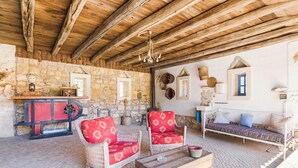 A rustic room with stone walls, wooden beams, wicker furniture, and a stone fireplace. - Refúgio das Artes (Porto de Mos)