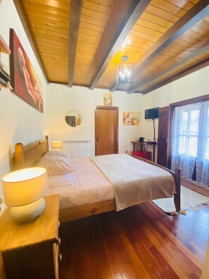 Ein Schlafzimmer mit Holzbalkendecke, einem Bett mit weißer Bettdecke, einer Nachttischlampe und einem Nachttisch aus Holz.