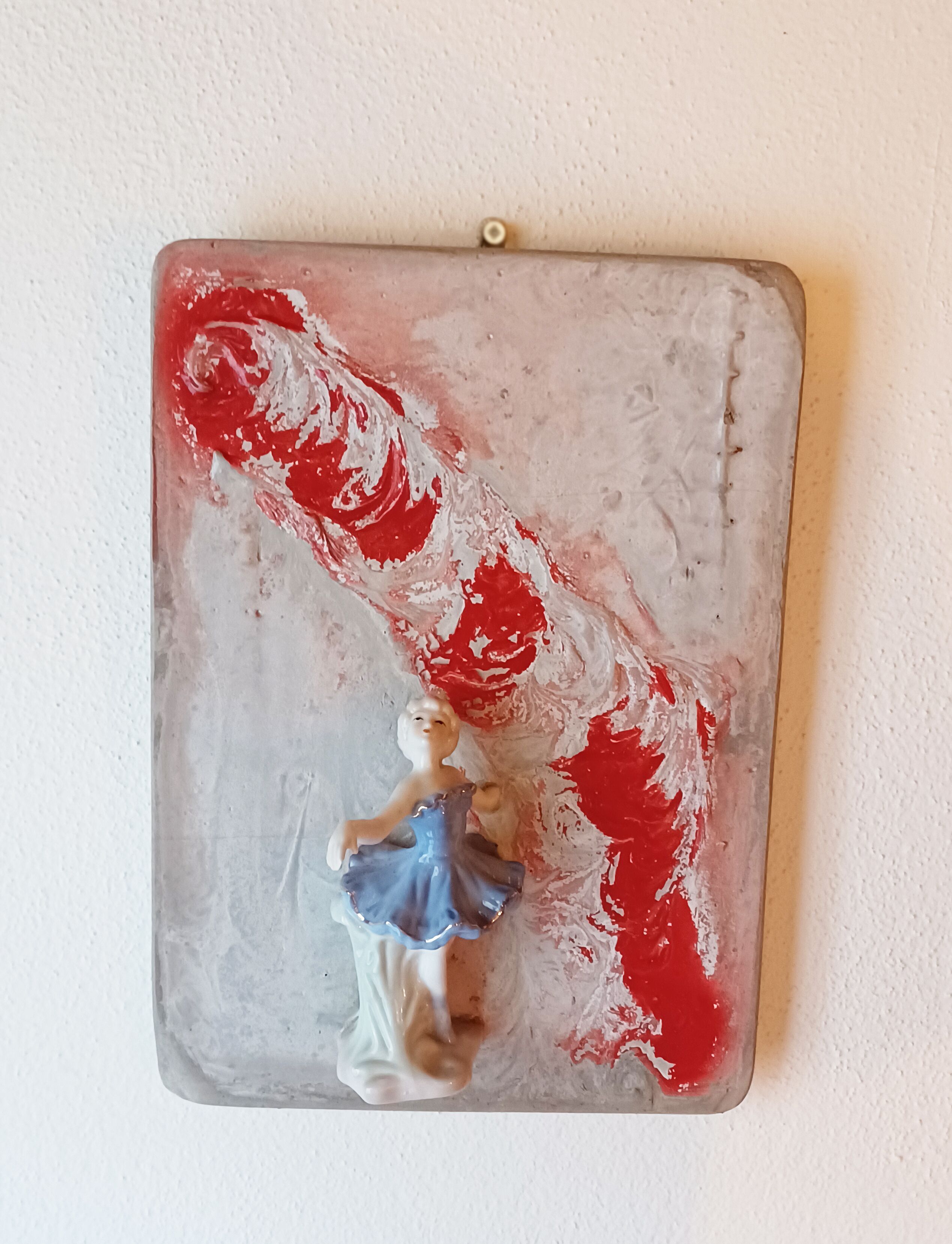 Una pieza decorativa montada en la pared con una figura y pintura abstracta roja y blanca.