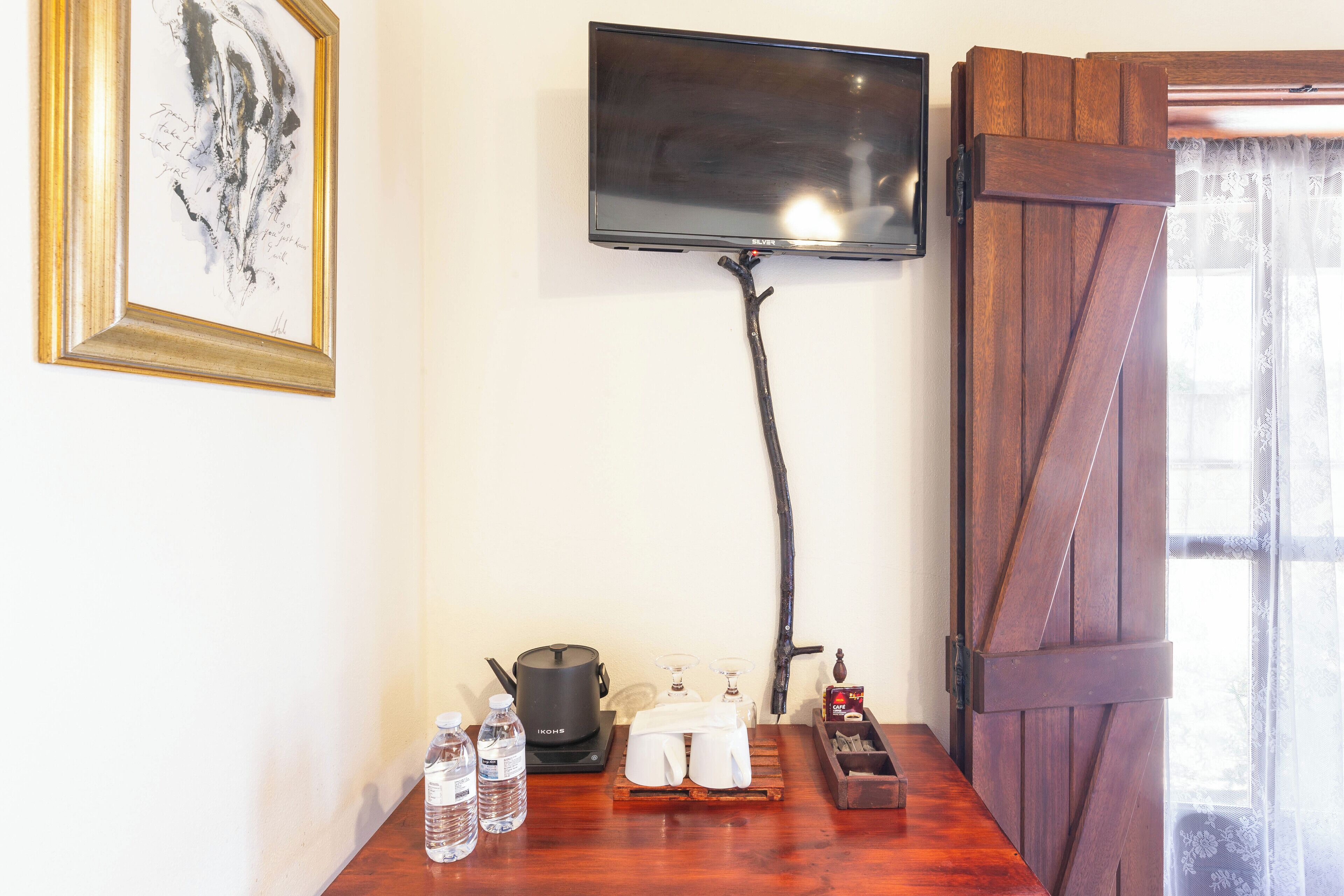 A room with a flat-screen TV mounted on the wall, a wooden door, a table with a kettle, glasses, and bottles.