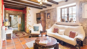 A cozy living room with a stone wall, wooden beams, a white sofa, a wooden coffee table, and a staircase leading to another level. - Refúgio das Artes (Porto de Mos)