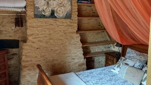 Una habitación rústica con una cama de madera, un muro de piedra y un dosel.