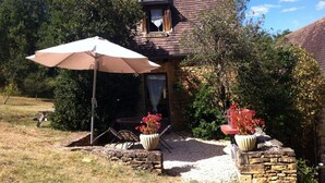 Una casa de piedra con techo de tejas, un balcón pequeño y un patio con mobiliario exterior y plantas en macetas.