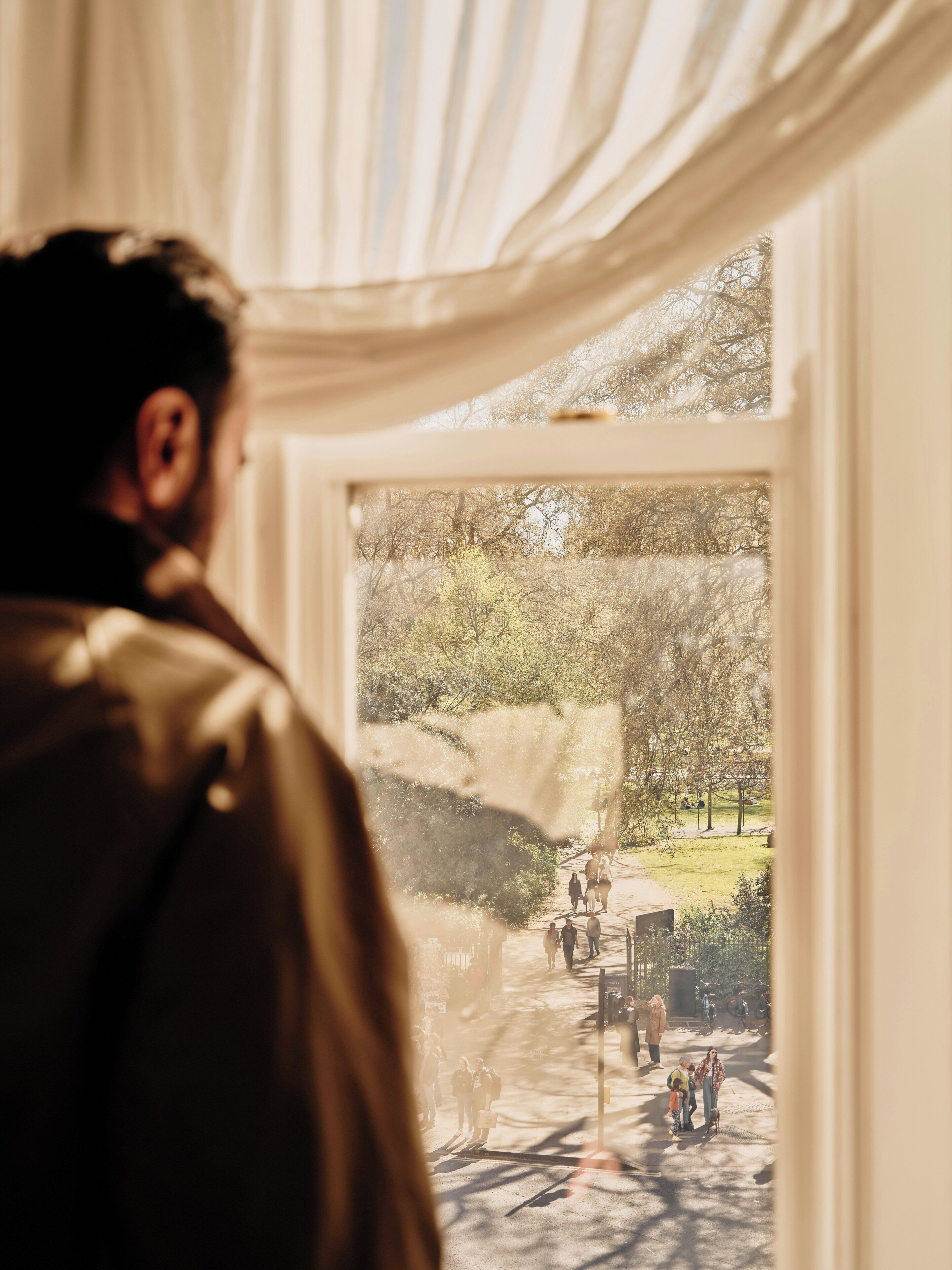 A person looking out of a window with a view of a park and people walking.