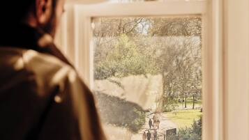 A person looking out of a window with a view of a park and people walking.