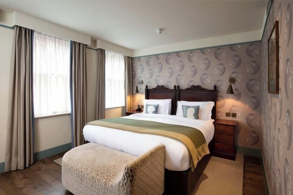 A hotel room with a large bed, a bedside table, a chair, and a patterned wall.