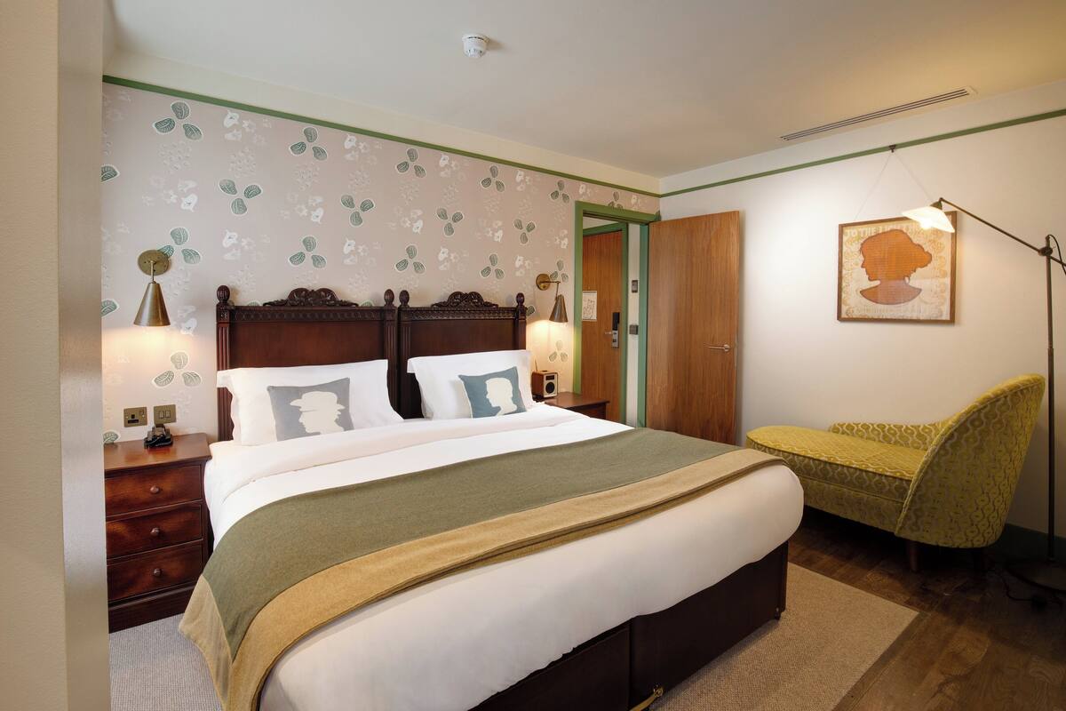 A neatly arranged bedroom with a large bed, bedside tables, a chair, and a wall-mounted lamp.