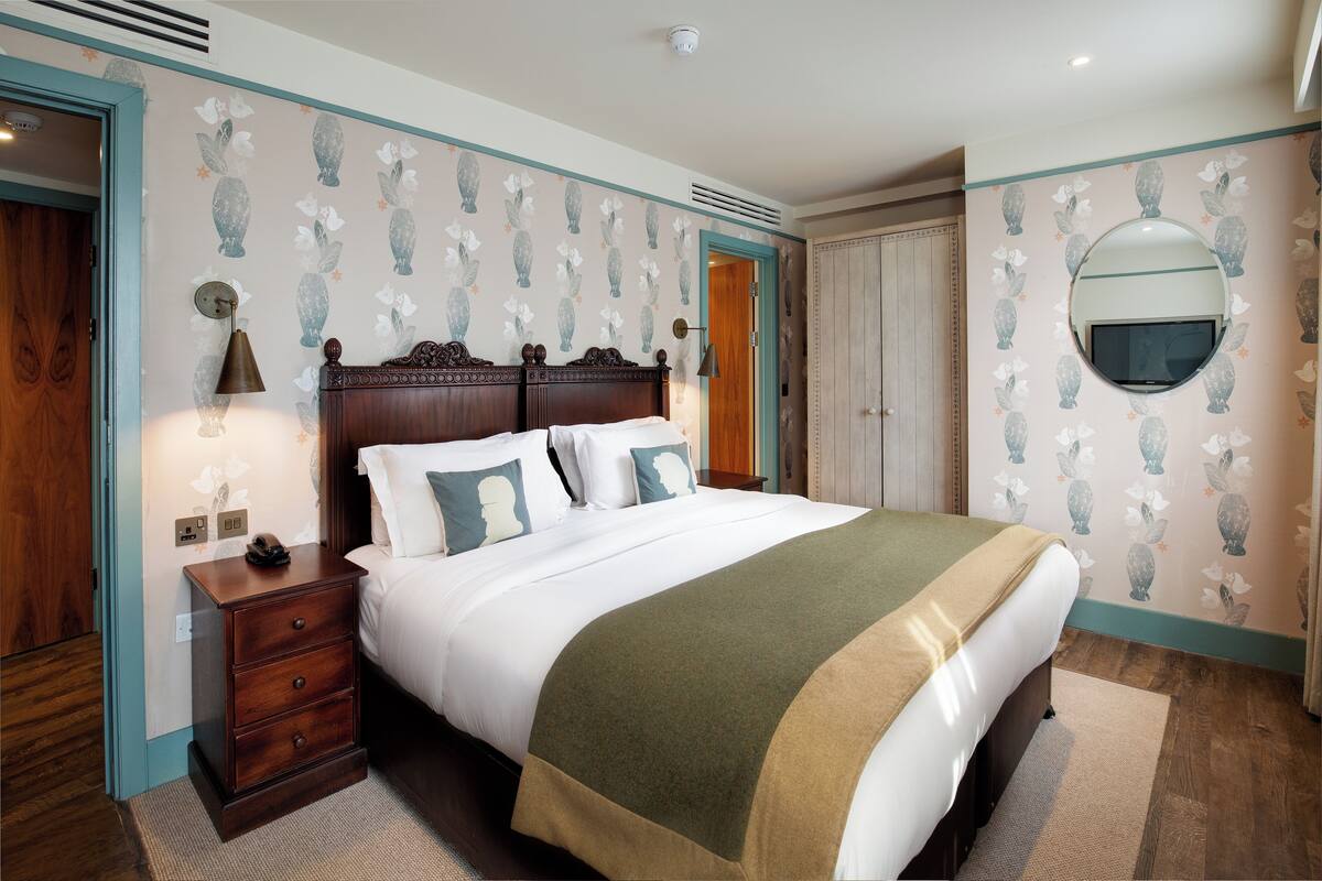A neatly arranged bedroom with a large bed, a bedside table, a mirror, and a wardrobe.