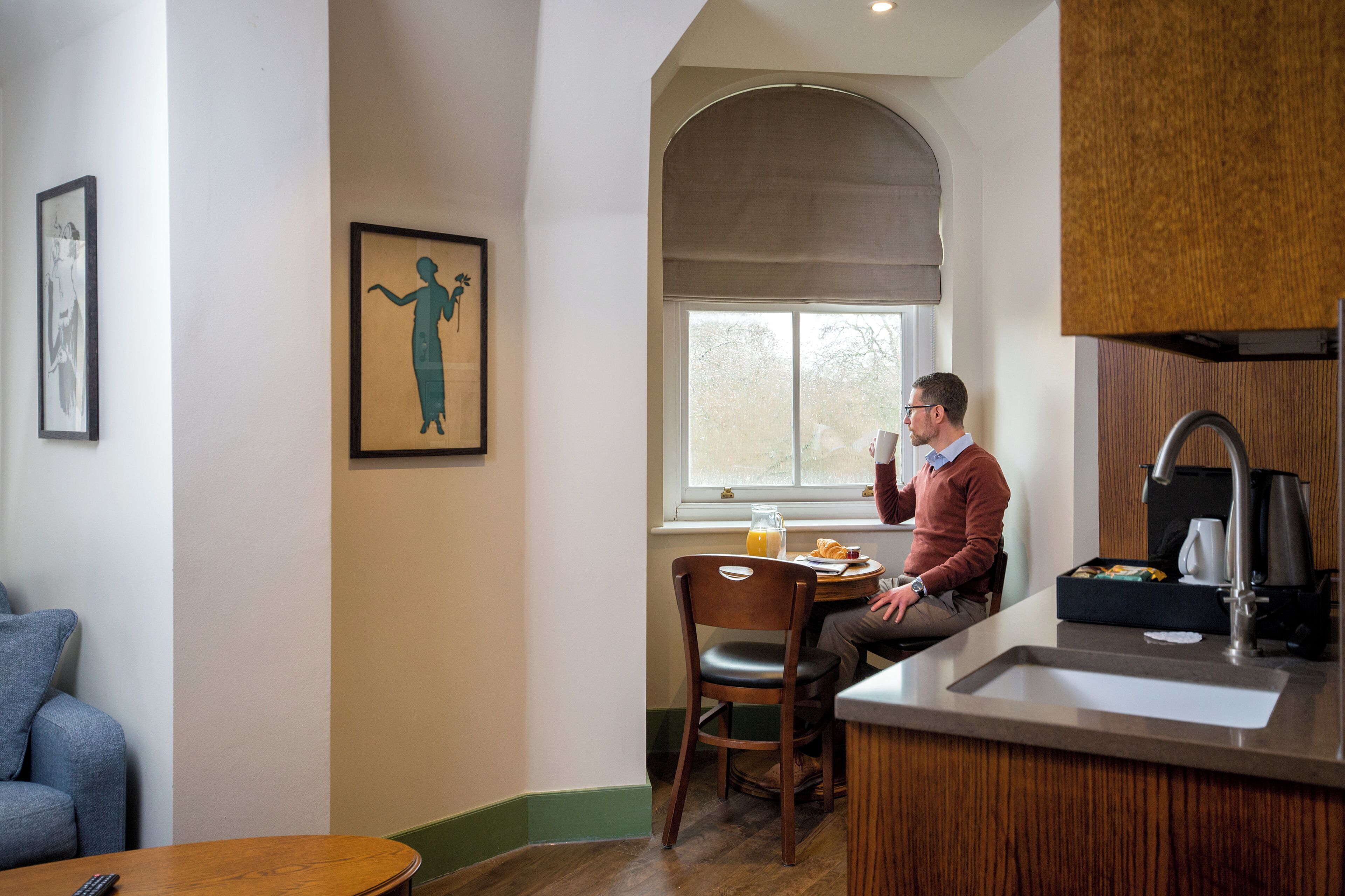 A kitchen with a window, a dining table, and a person sitting at the table.