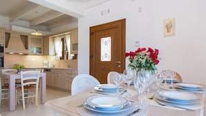 Un coin repas avec une table en bois dressée pour quatre personnes, entourée de chaises. Un vase rempli de fleurs est posé sur la table.