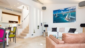 A modern living room with a sofa, a dining area with chairs, a staircase, and a large painting of sailboats on the wall. - Superb house with sea view, 3 bedrooms, 3 bathrooms, jacuzzi, sauna, Old Town (Antibes)