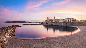 A coastal town with a historic building complex by the sea, a calm beach, and a clear sky. - Superb house with sea view, 3 bedrooms, 3 bathrooms, jacuzzi, sauna, Old Town (Antibes)