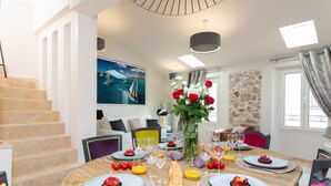 A dining area with a wooden table set for a meal, a staircase, a painting of a sailboat, and a stone wall. - Superb house with sea view, 3 bedrooms, 3 bathrooms, jacuzzi, sauna, Old Town (Antibes)