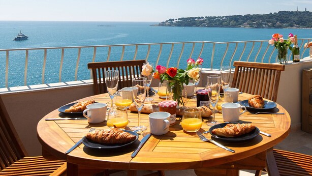 A round wooden table with breakfast items, a view of the sea, and a balcony with a sofa and chairs. - Superb house with sea view, 3 bedrooms, 3 bathrooms, jacuzzi, sauna, Old Town (Antibes)