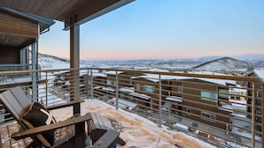 Terraza de madera con vista a montañas nevadas y edificios.
