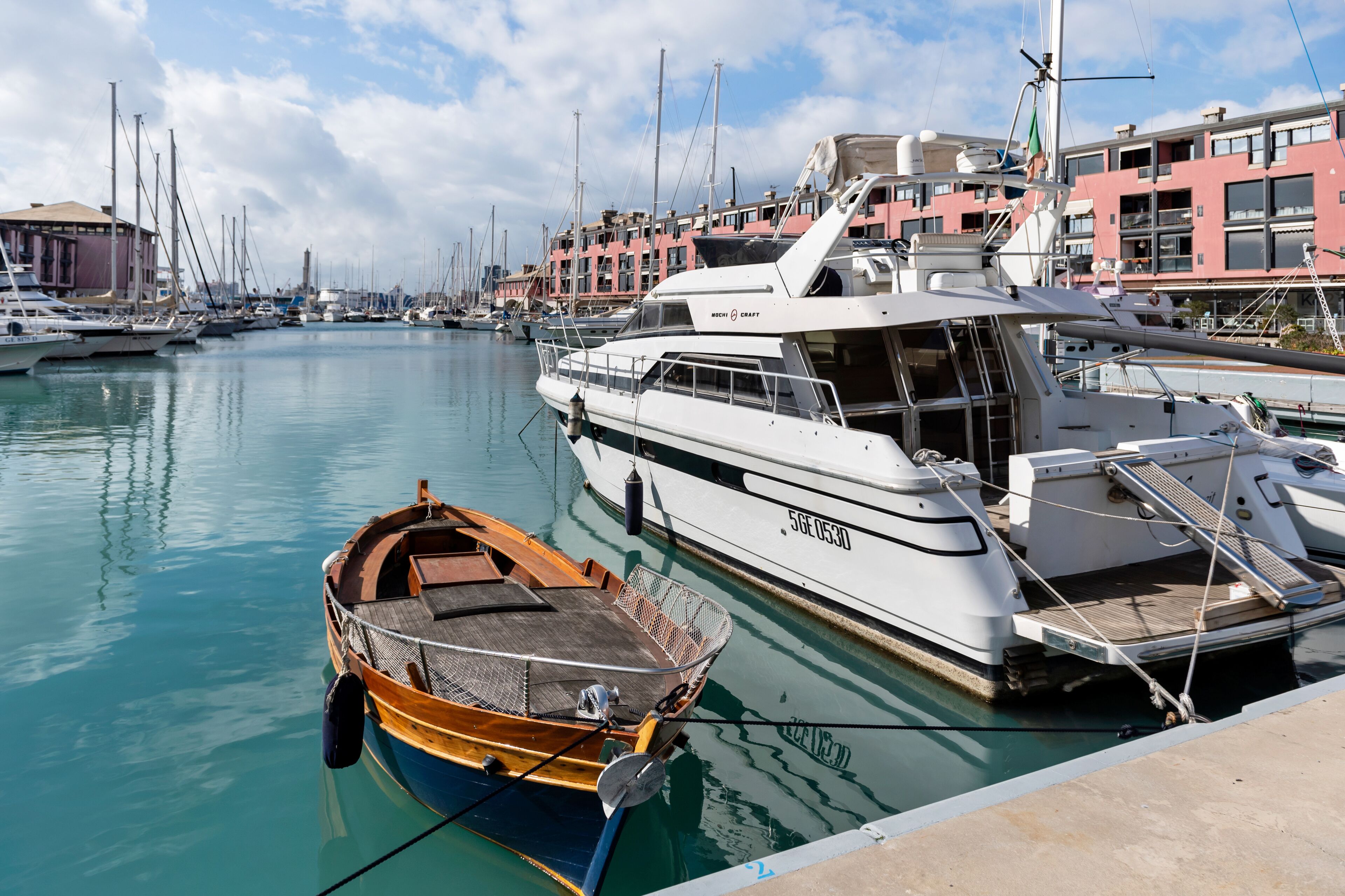 A marina with various boats docked, including a small rowboat and a larger yacht.