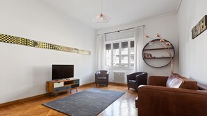 Un salon avec un téléviseur, des fauteuils en cuir, un canapé marron, un tapis gris et un plancher en bois.