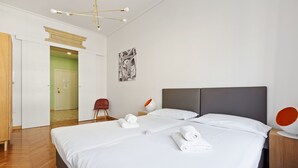 Une chambre d’hôtel avec un grand lit, une armoire en bois, un bureau avec une chaise et une porte donnant sur une autre pièce.