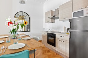 Een moderne keuken met een houten eettafel, roestvrijstalen apparatuur en een vaas met bloemen.