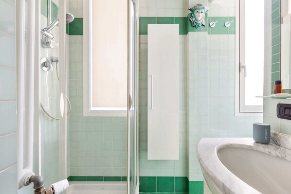 A bathroom with a glass shower enclosure, a white vanity with a marble countertop, and a green-tiled wall. - Gambara Cosy Apartment (Milan)