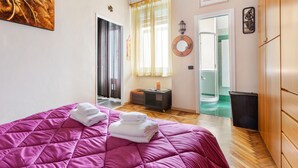 A bedroom with a pink bedspread, a small bedside table with a lamp, a mirror, and a door leading to a bathroom. - Gambara Cosy Apartment (Milan)