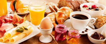 Una mesa de desayuno con croissants, huevos, mermelada y café.
